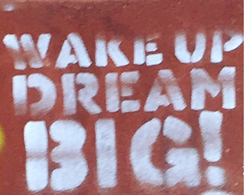 WAKE UP DREAM BIG, white graffiti painted in block letters on an orange, cement wall in NYC